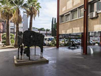 Scendiamo di nuovo nell'atrio e usciamo dalla parte opposta passando sotto un altro porticato. Tra le colonne sono disseminate alcune sculture informali di artisti contemporanei: ammiriamo per esempio la capanna di bronzo stilizzata di Alfio Castelli...